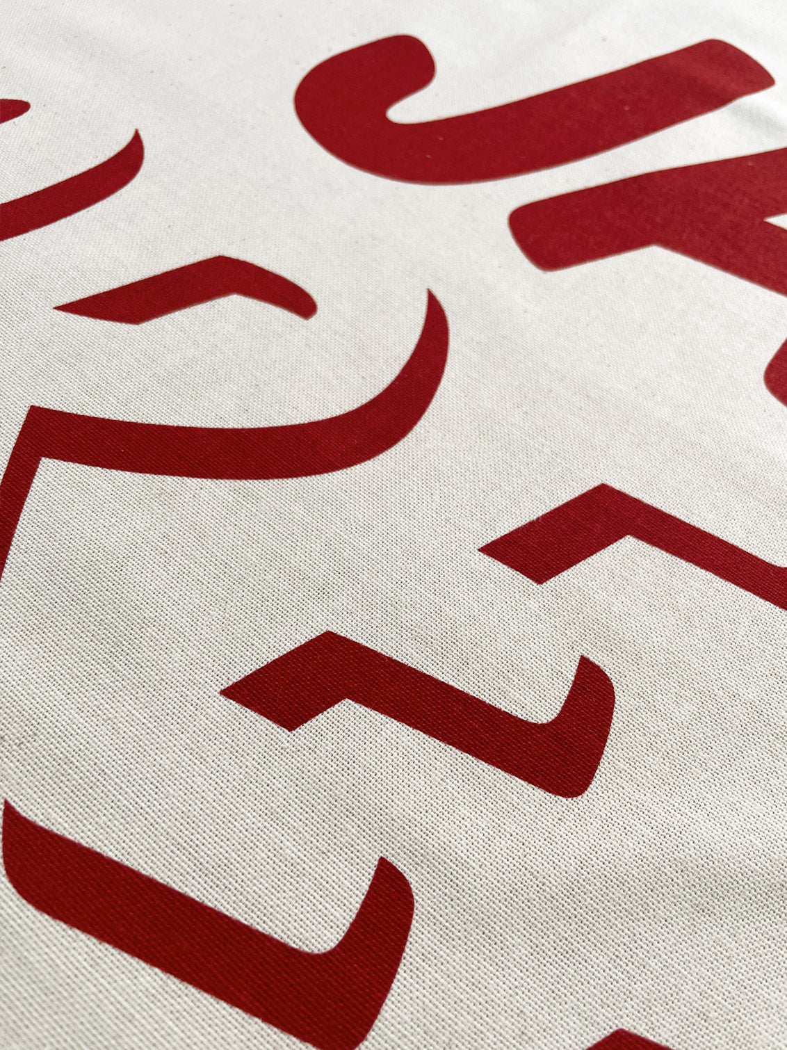 Close up of the red ink printed lettering on the cream natural cotton teatowel fabric.