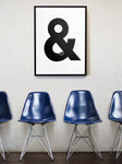 A framed monochrome print hangs on white wall above a row of Eames chairs in blue, The picture is a screenprint of an ampersand with a china cup and a biscuit made out of the negative space. It reads visually as Tea and Biscuits