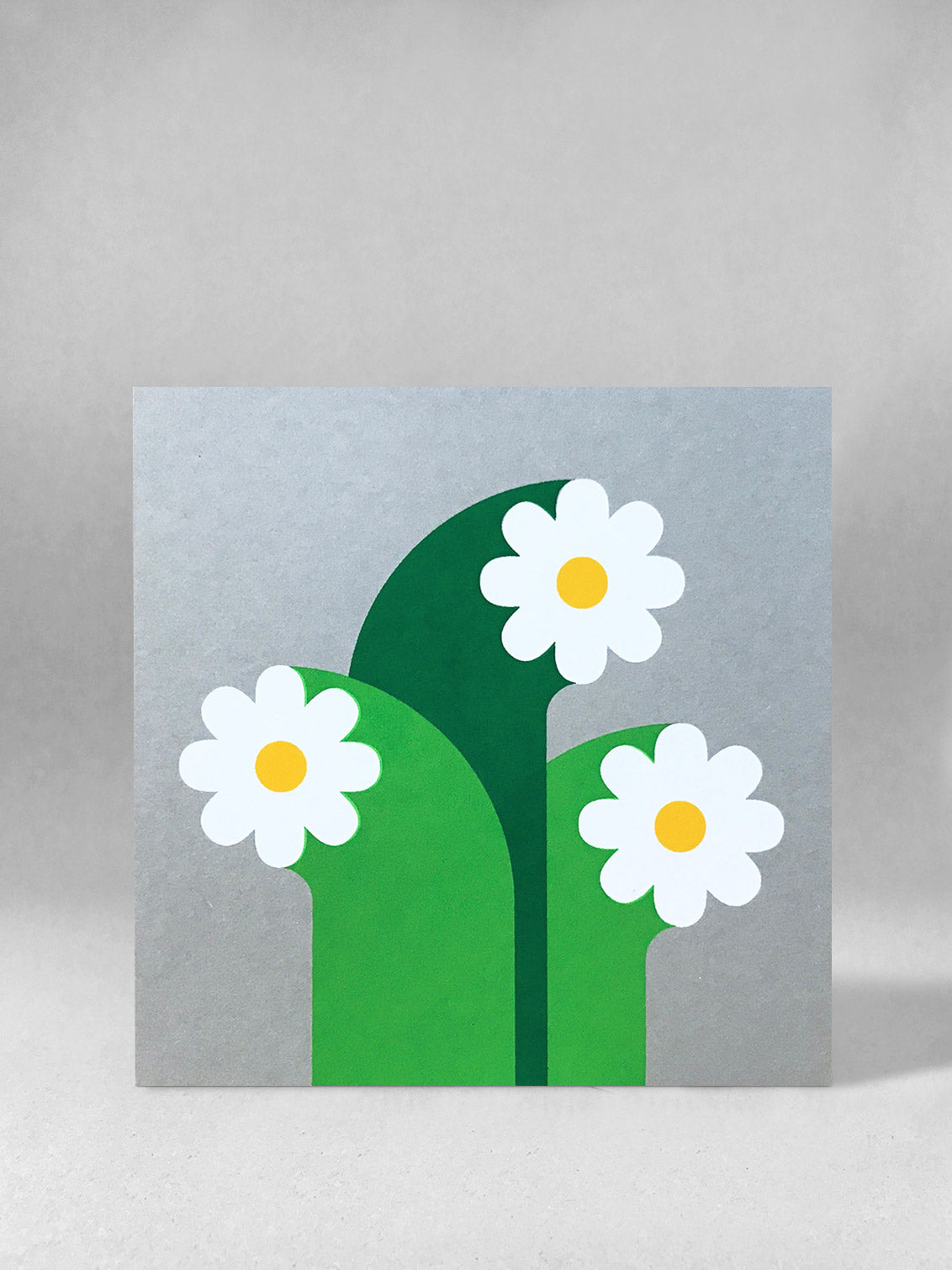  Three white flowers with graphic wide stalks and golden yellow circle centres, screenprinted onto grey card, stood front on in a light grey studio shot.