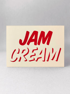 Cleanly printed type in strawberry red ink on a cream coloured recycled card stock, reading CREAM across the bottom with JAM written on top! Card stood front on in a light grey studio set.