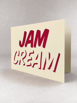 Cleanly printed type in strawberry red ink on a cream coloured recycled card stock, reading CREAM across the bottom with JAM written on top! Card stood slightly open in a light grey studio set.
