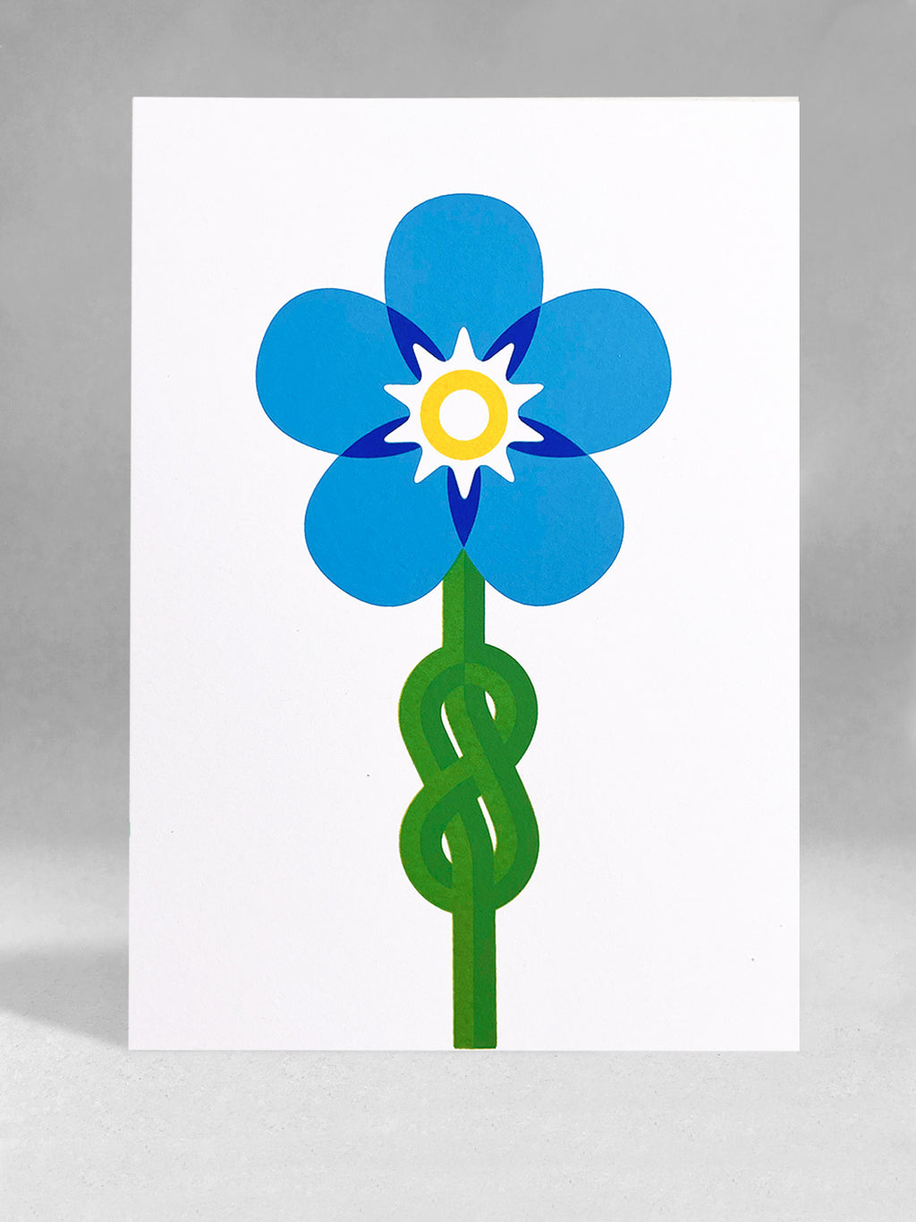 A forget me knot image using 5 colours blues, yellow and green screenprinted onto a white portrait card, stood in a light grey studio backdrop.