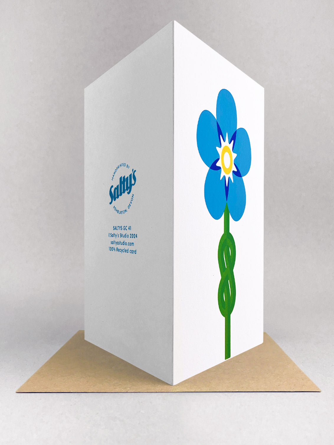 Rear view of a portrait greetings card, with a forget me knot image designed in minimal graphic style, using 5 colours blues, yellow and green screenprinted onto a white portrait card, stood in a light grey studio backdrop on a kraft envelope