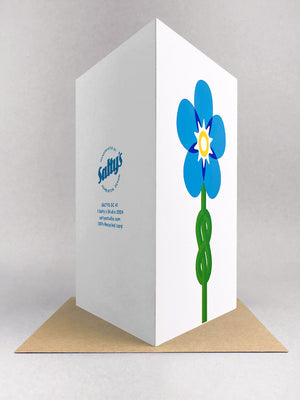 Rear view of a portrait greetings card, with a forget me knot image designed in minimal graphic style, using 5 colours blues, yellow and green screenprinted onto a white portrait card, stood in a light grey studio backdrop on a kraft envelope