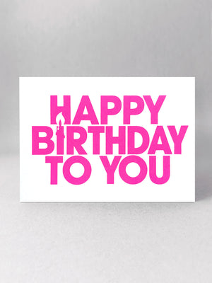 Happy Birthday to You landscape greetings card. The I of Birthday is a candle using negative space. A front on view - Printed in capital letters, simple font printed in neon pink ink on a white card made by Salty's Studio.