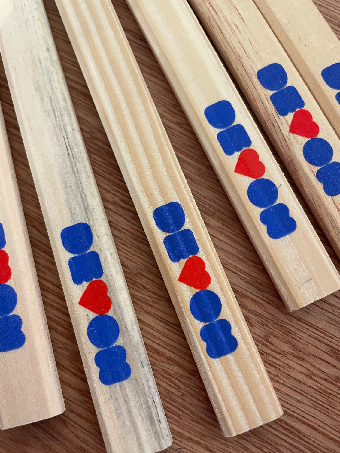 Carpenters pencils lying on a wooden table top, unsharpened. The printed word of Devon, with the V as a heart and in royal blue and red is shown across all of them.