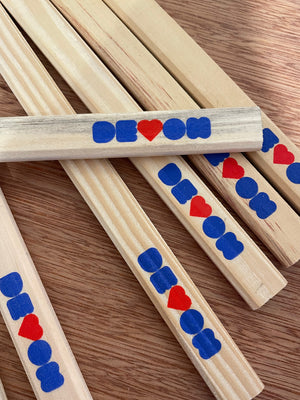 Carpenters pencils lying on a wooden table top, one pencil lies across the majority. The printed word of Devon, with the V as a heart is in royal blue and red is shown across all of them.