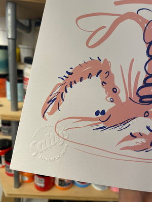 Close up of an embossed Salty’s logo, saying handprinted in Ashburton, overlapped with the face and claw of a screenprinted langoustine. 