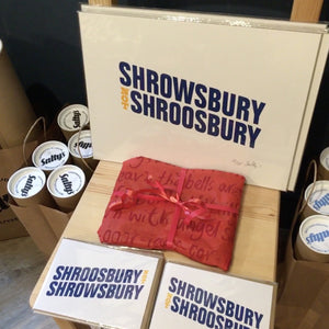 ShrOWsbury not ShrOOsbury screen print on a chair with a red present wrapped in handprinted paper. Cardboard tubes of prints in a bag to one side. more Shrewsbury cards in the foreground.