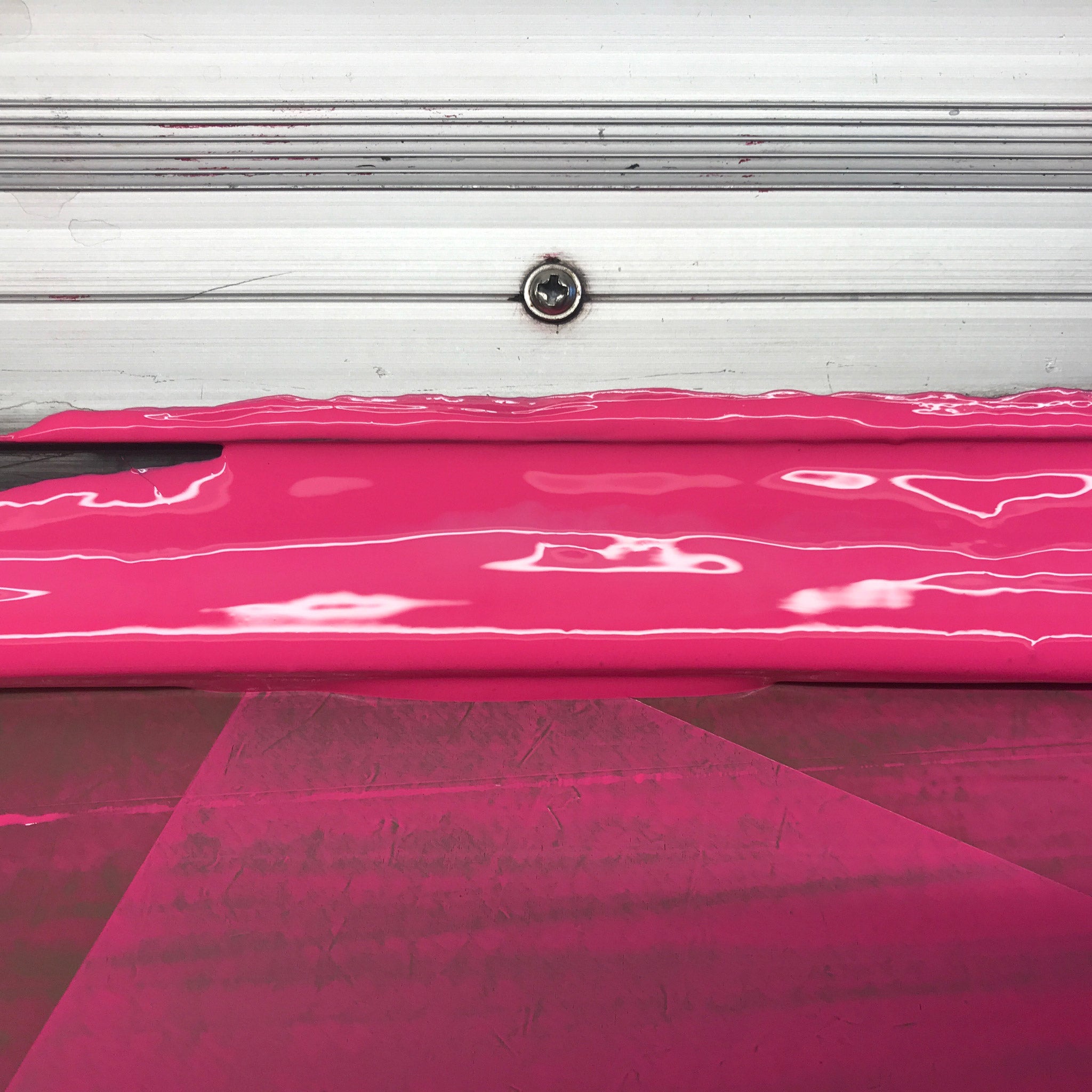 Extreme close up of a screenprinting squeegee loaded with bright pink ink. Aluminium at the top, a bolt and then a shiny expanse of pink ink.