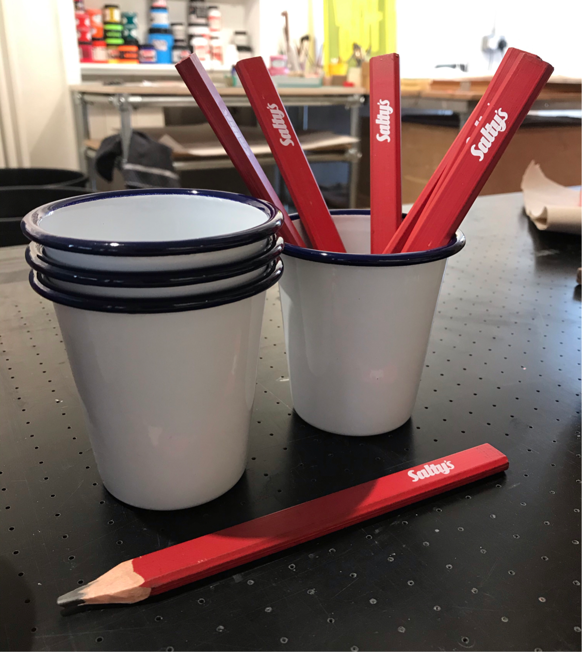 Some red carpenters pencils in white Falconware tumbler pots. Sat on a print table and pots of ink in the background.