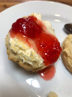 A scone on a white ceramic plate with Devon clotted cream on the bottom, then strawberry jam dolloped on top. The right way to eat a cream tea ;)